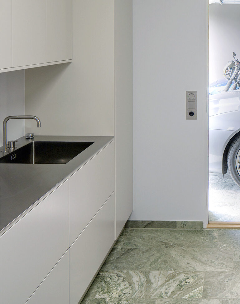 Vaskerom med benkeplate i rustfritt stål, integrert vask og lyse fronter i Villa Svanshall