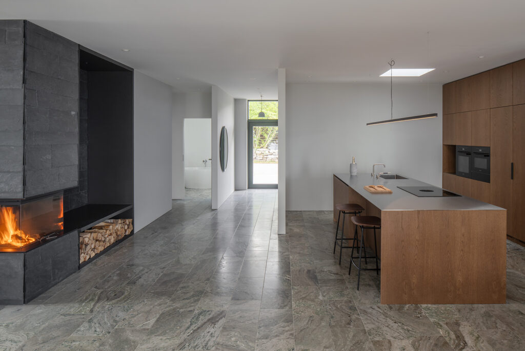 Kjøkken i rustfritt stål i åpen stue- og kjøkkenløsning med peis og naturmaterialer i Villa Svanshall